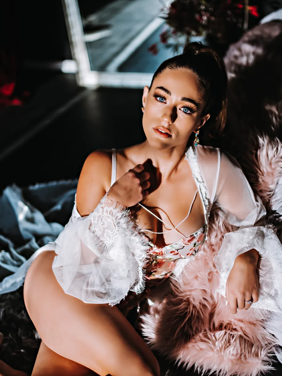 Brunette client in a white and blush feather robe seated among soft furs