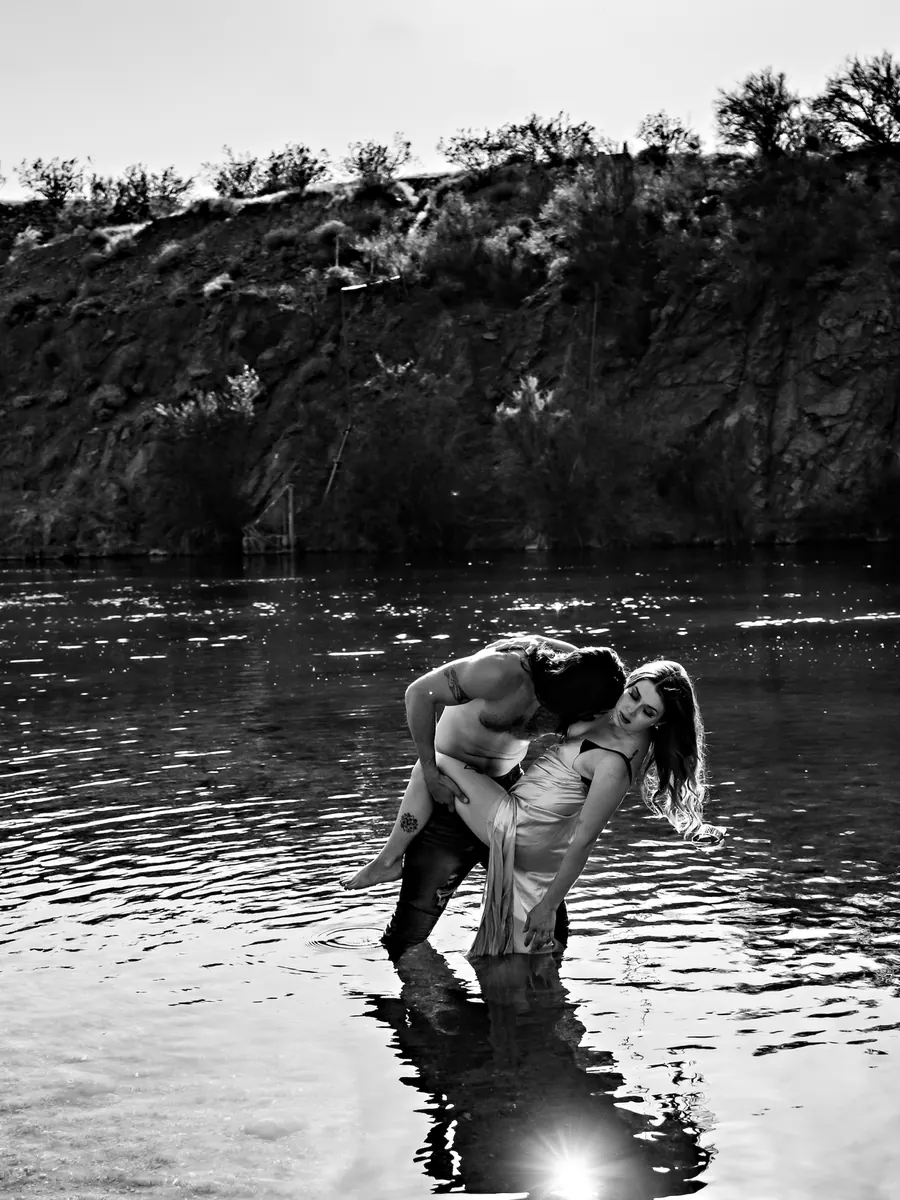 Black-and-white wide shot of a couple embracing in a desert river