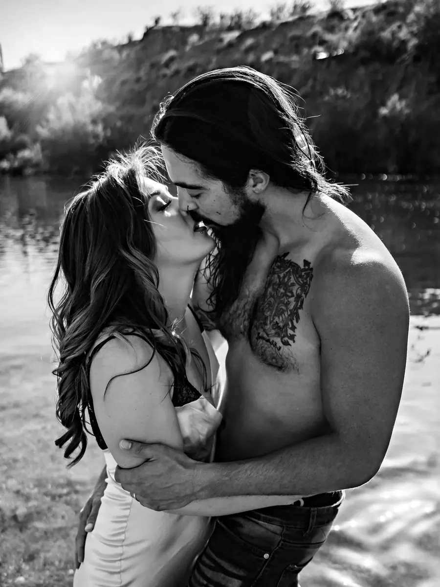 Black-and-white portrait of a couple kissing beside a desert river