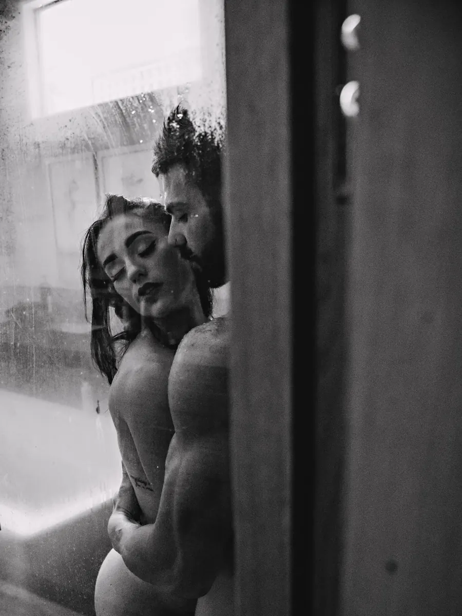 Black-and-white portrait of a couple embracing behind misted shower glass