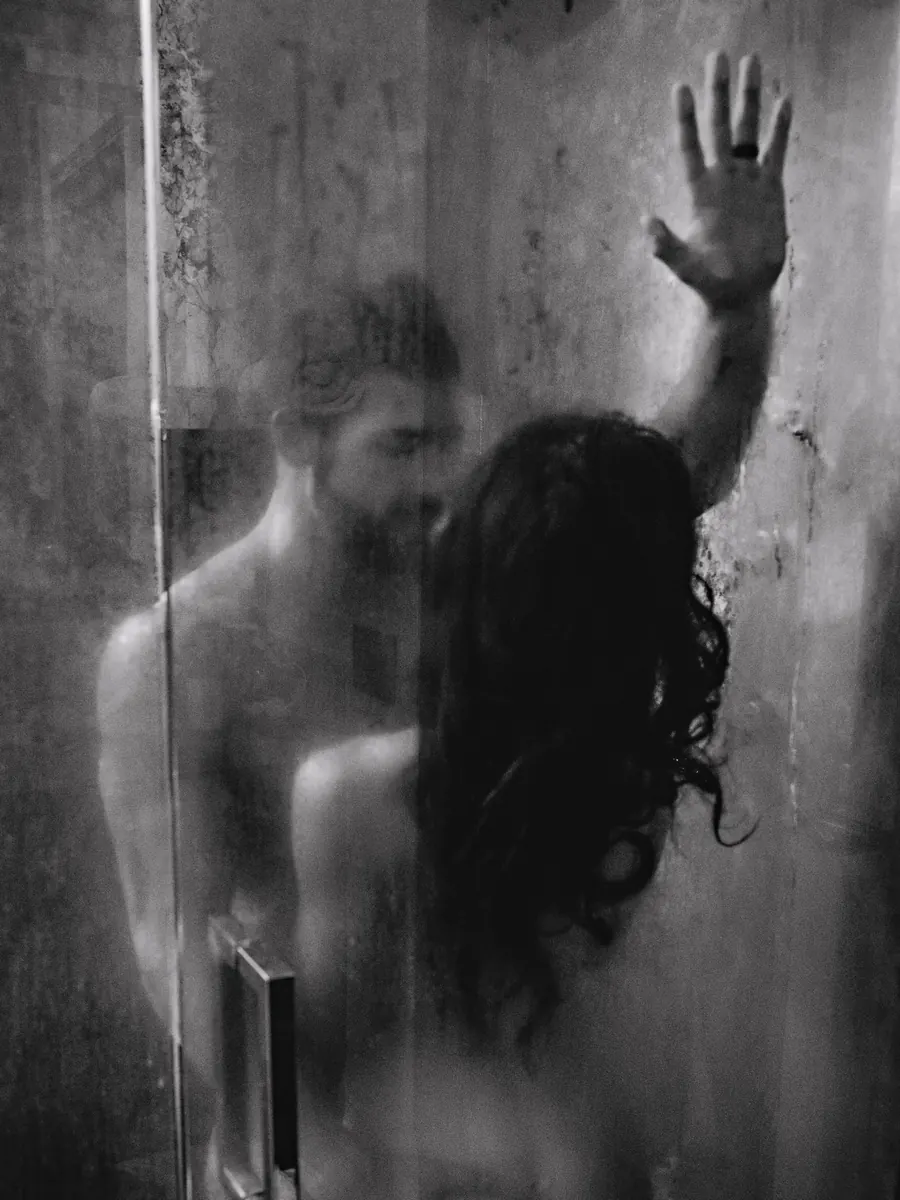 Black-and-white portrait of a couple in the shower, her hand pressed to the glass