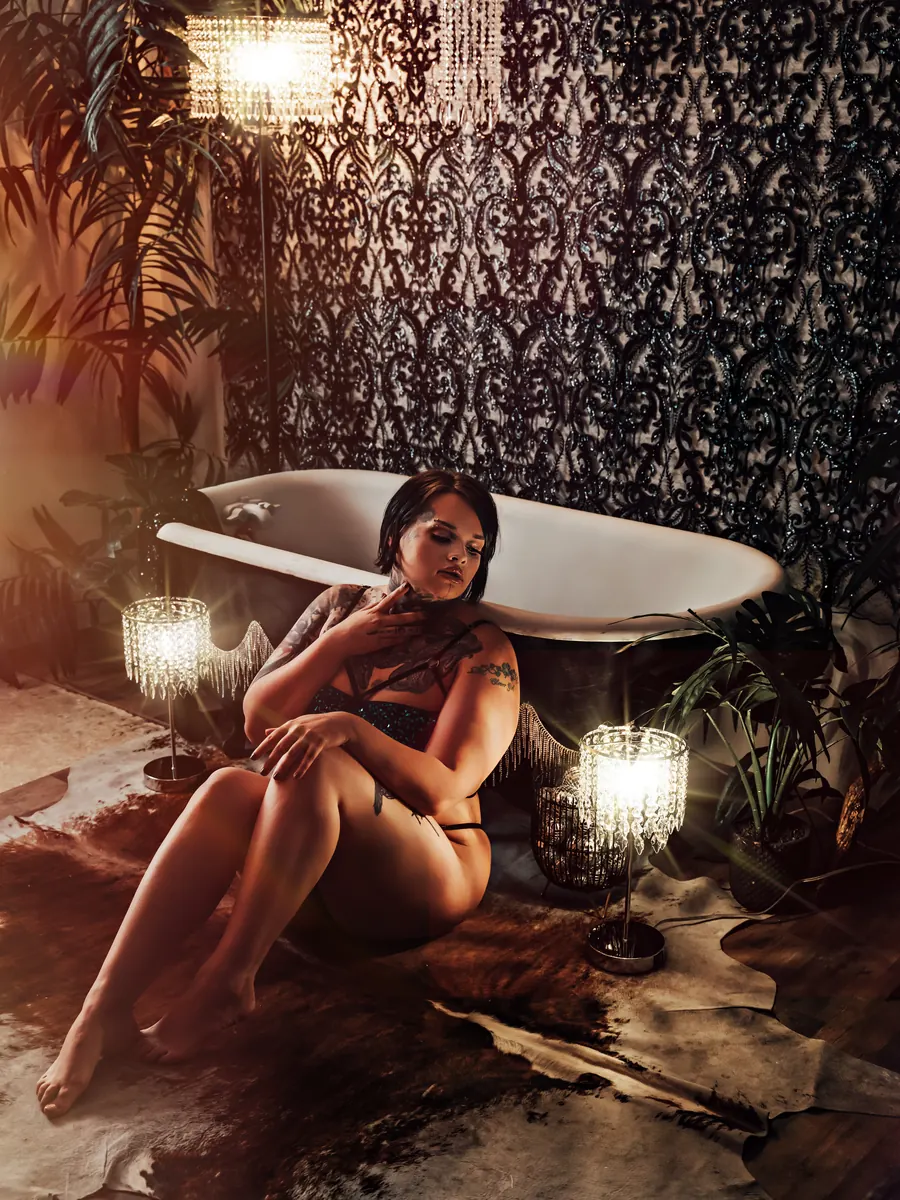 Client seated on a cowhide rug beside a clawfoot tub and candles against damask wallpaper