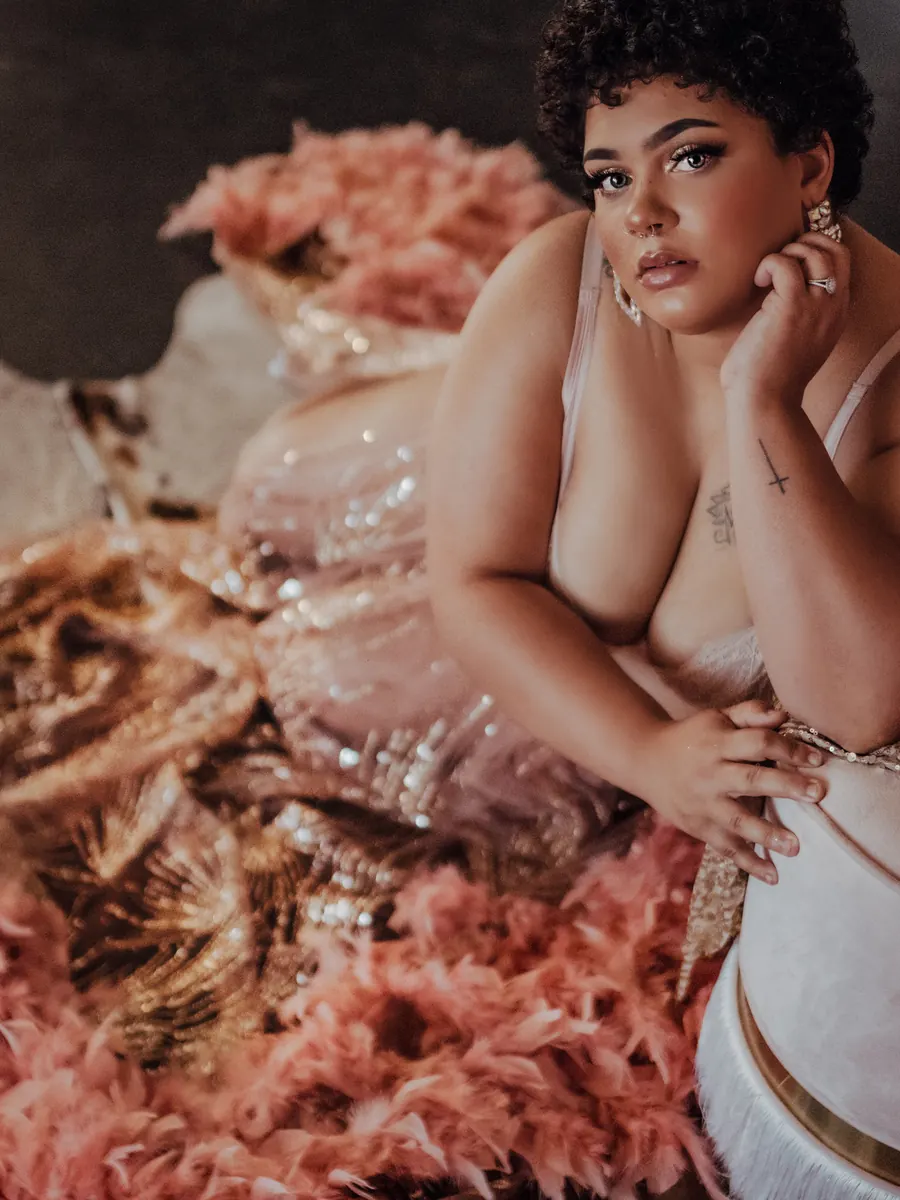 Client with short curls in a gold sequin gown, reclining on a bed of pink feathers