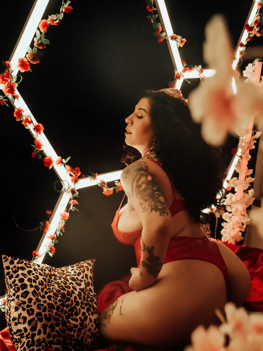 Tattooed client in red lingerie kneeling on red satin beneath hexagon light panels