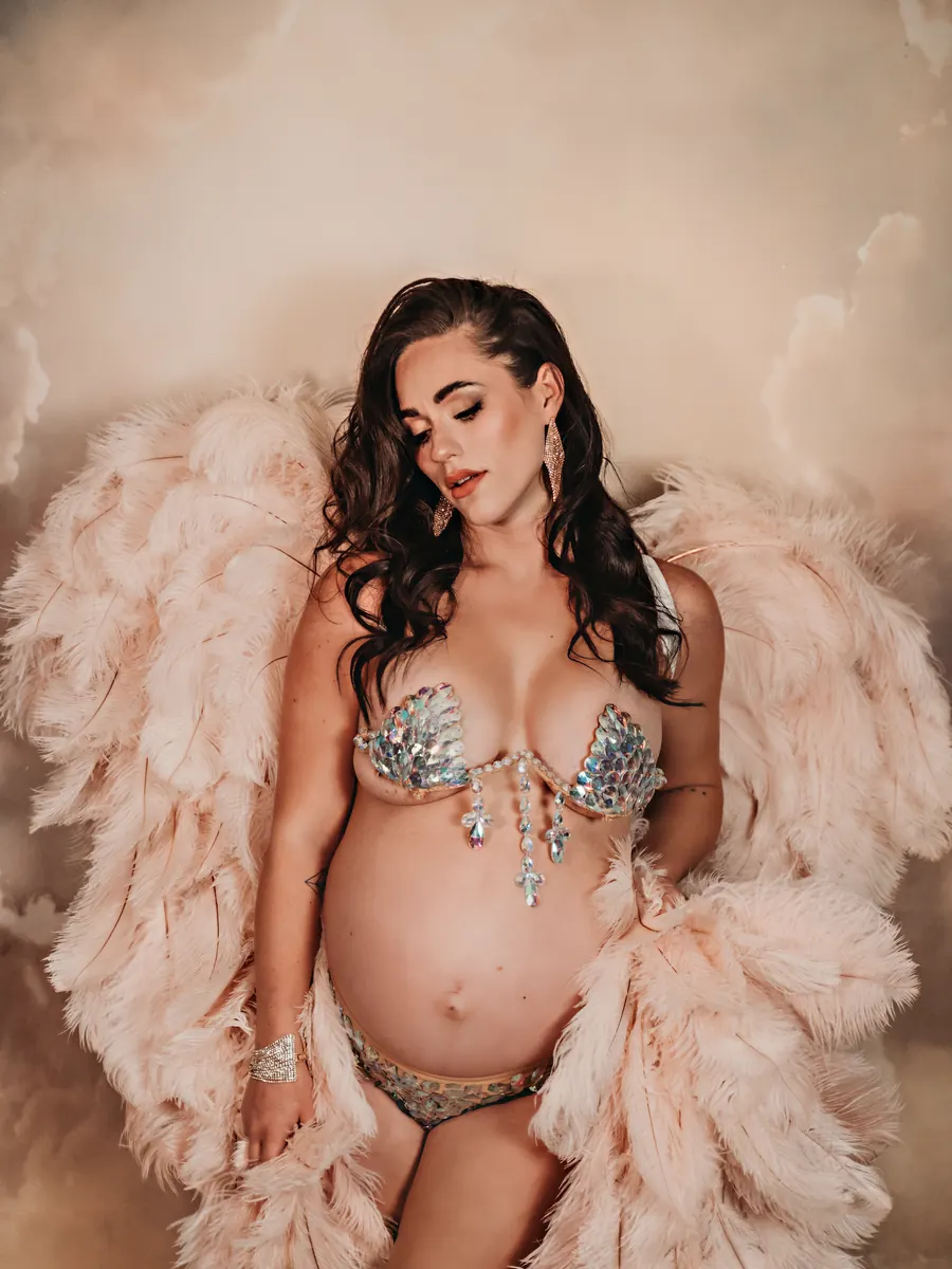 Expectant mother in a jewelled bralette and blush feathered wings