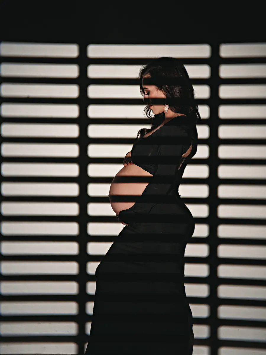 Profile of an expectant mother in black against striped window-blind light