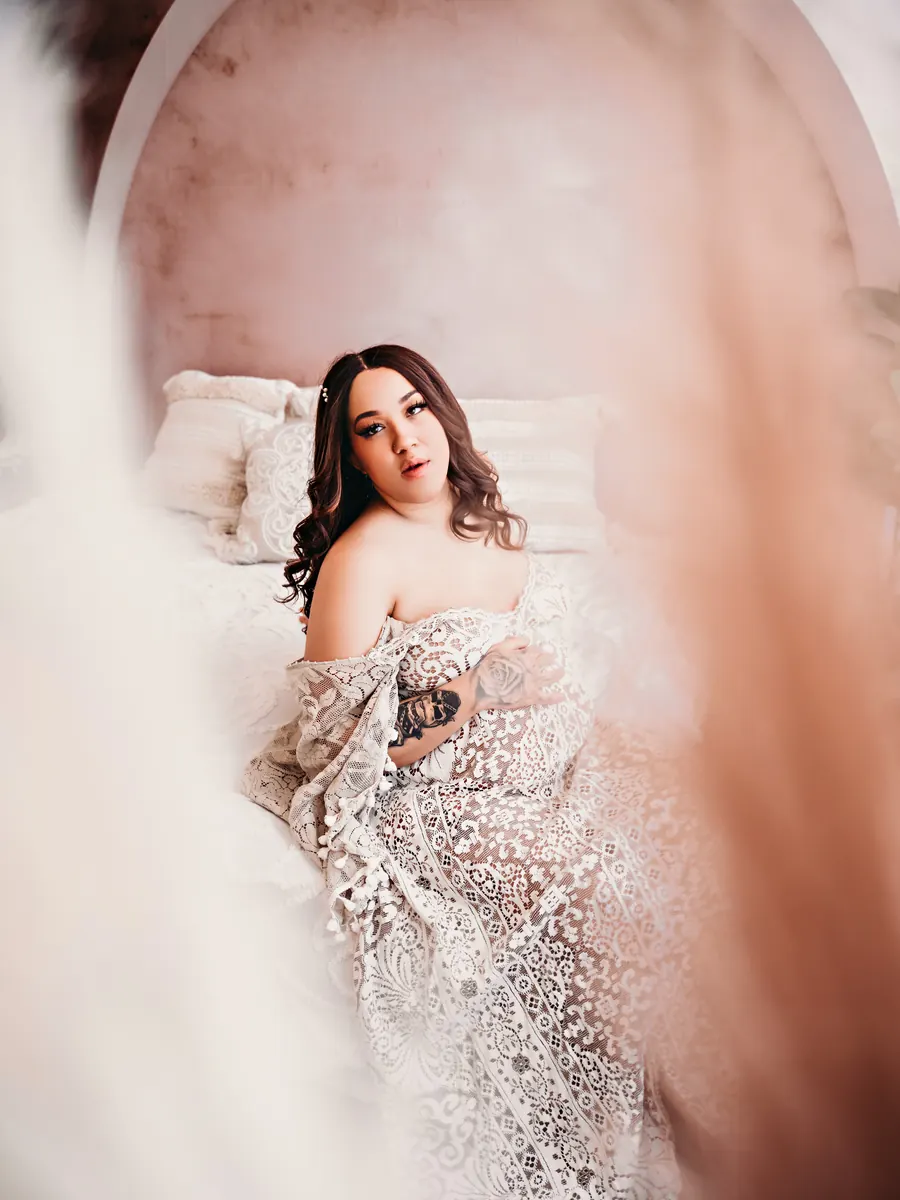 Expectant mother in a sheer lace robe framed by soft blush light