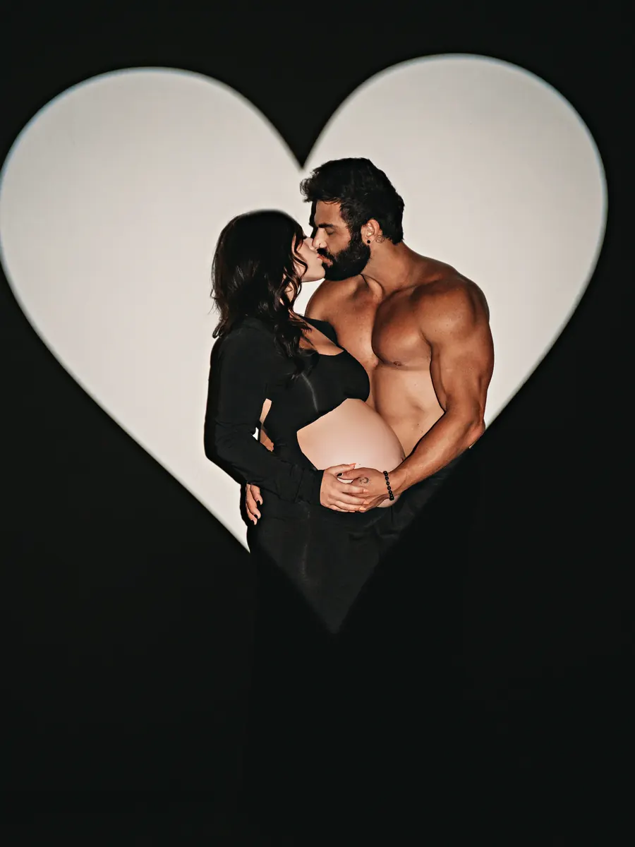 Expectant mother and her partner kissing inside a glowing heart-shaped silhouette