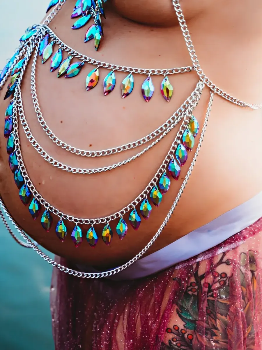 Close detail of a pregnant belly draped in iridescent jewelled body chains beside blue water