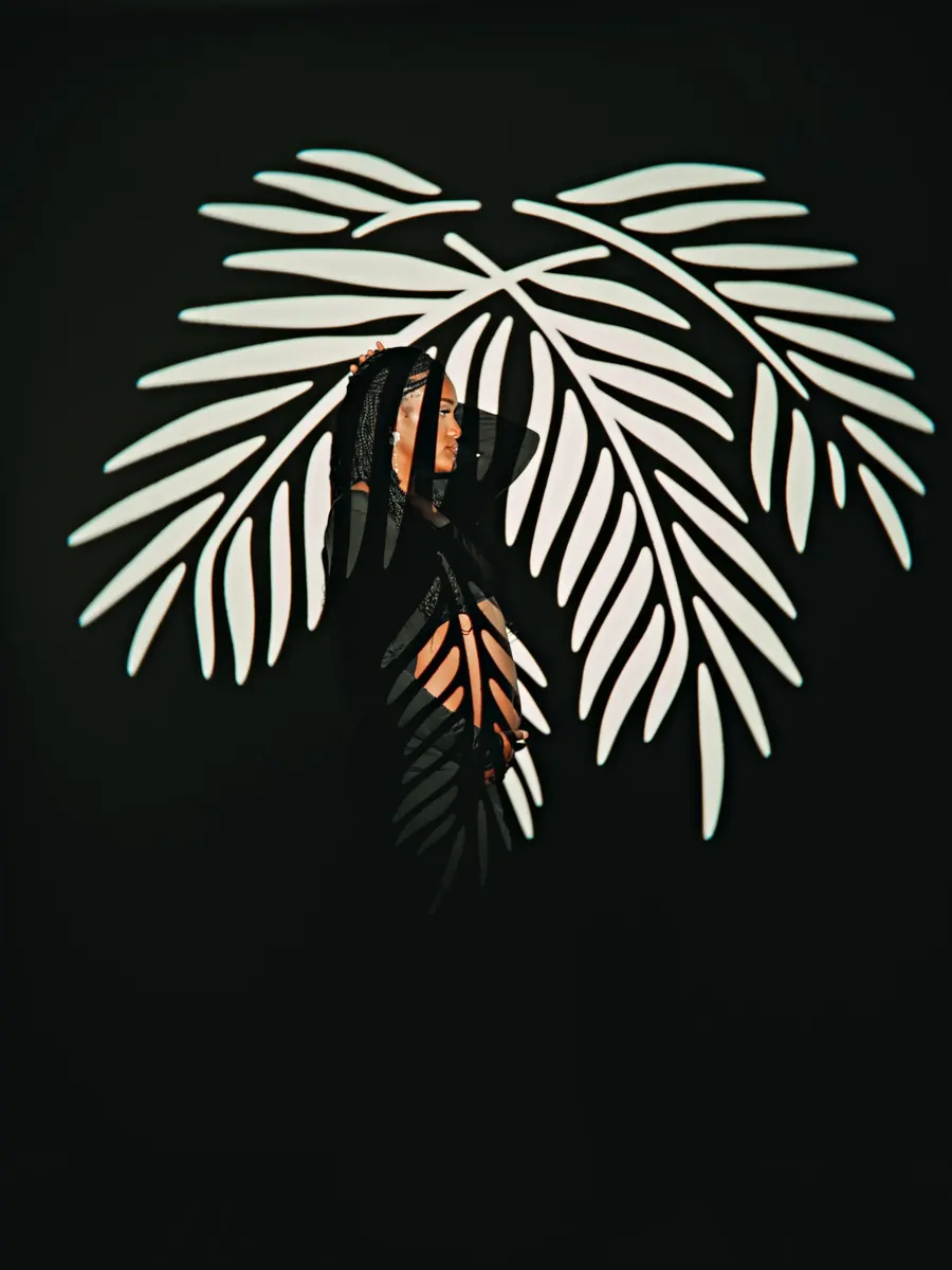 Expectant mother in shadow behind a sculptural white palm leaf on black