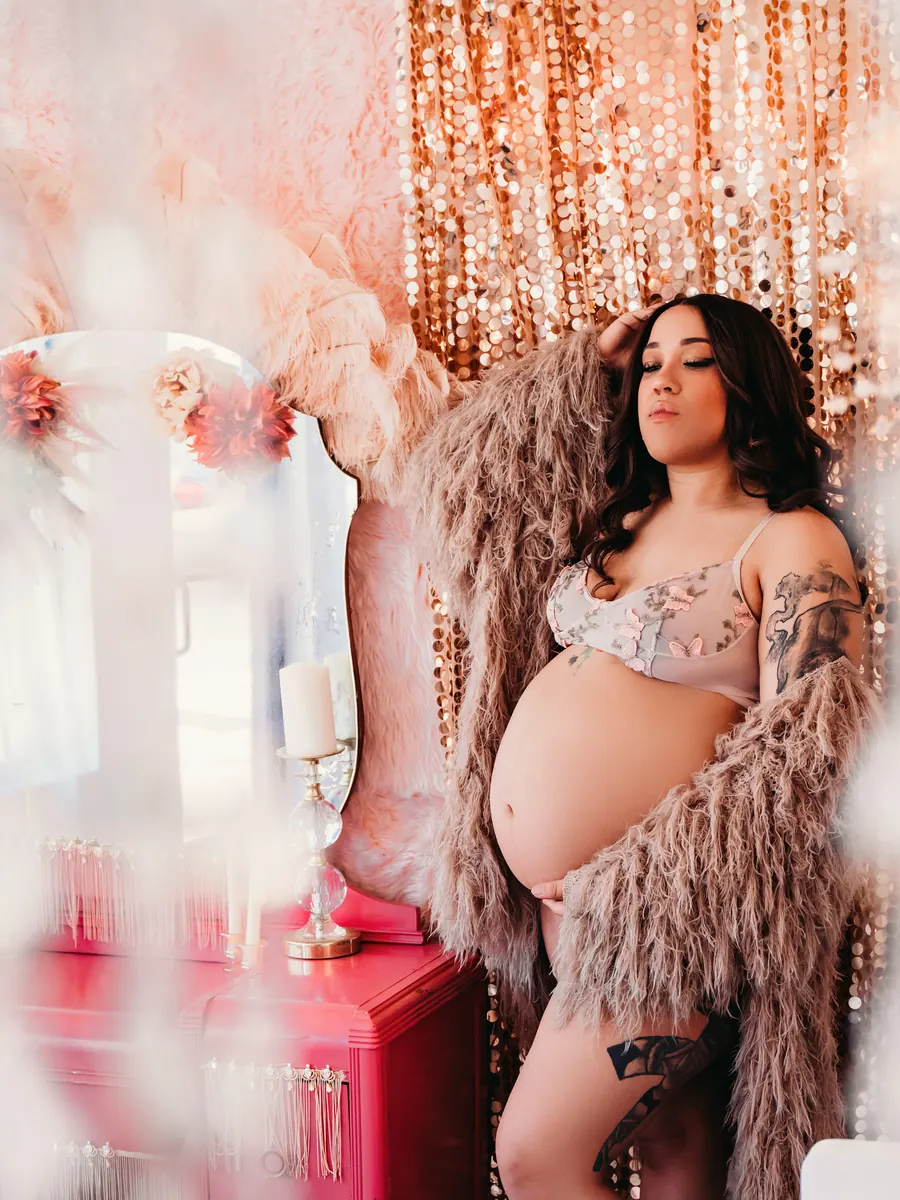 Expectant mother in a feathered wrap before rose-gold sequin curtains