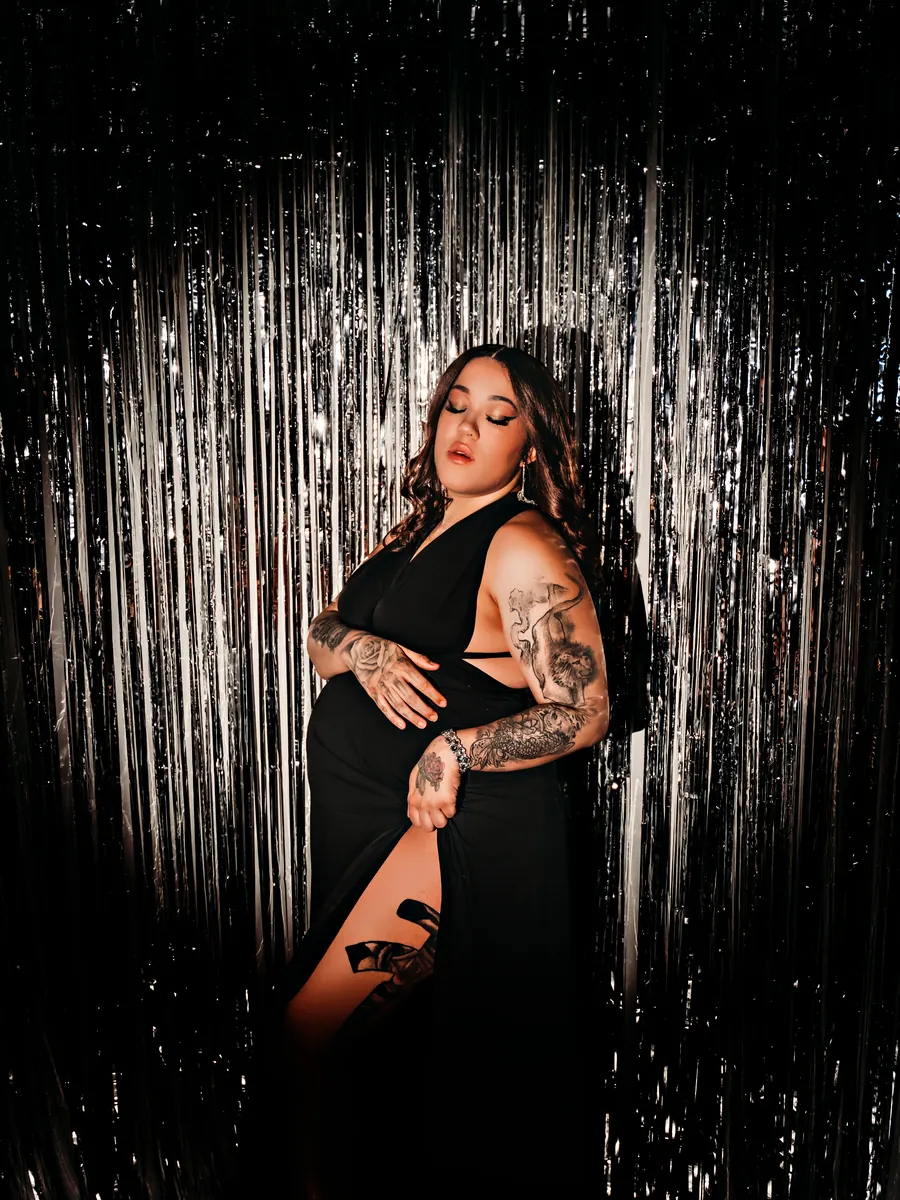 Expectant mother in a black gown against a silver streamer backdrop