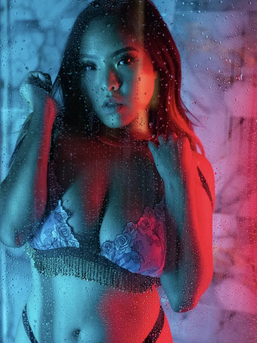 Client in a lace bralette behind rain-streaked glass, lit in blue and red neon