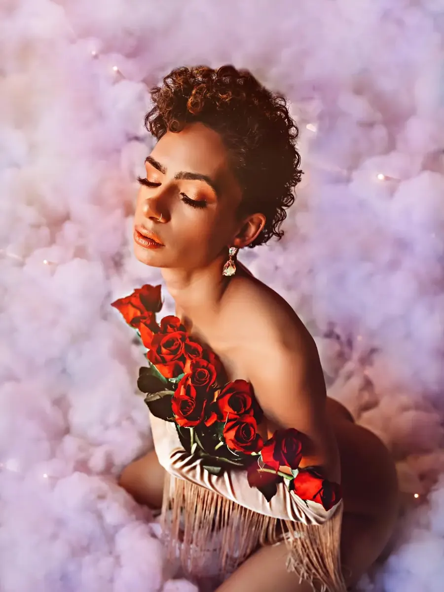 Client with short curls in a rose-covered fringed bodysuit, surrounded by soft pink and lilac clouds
