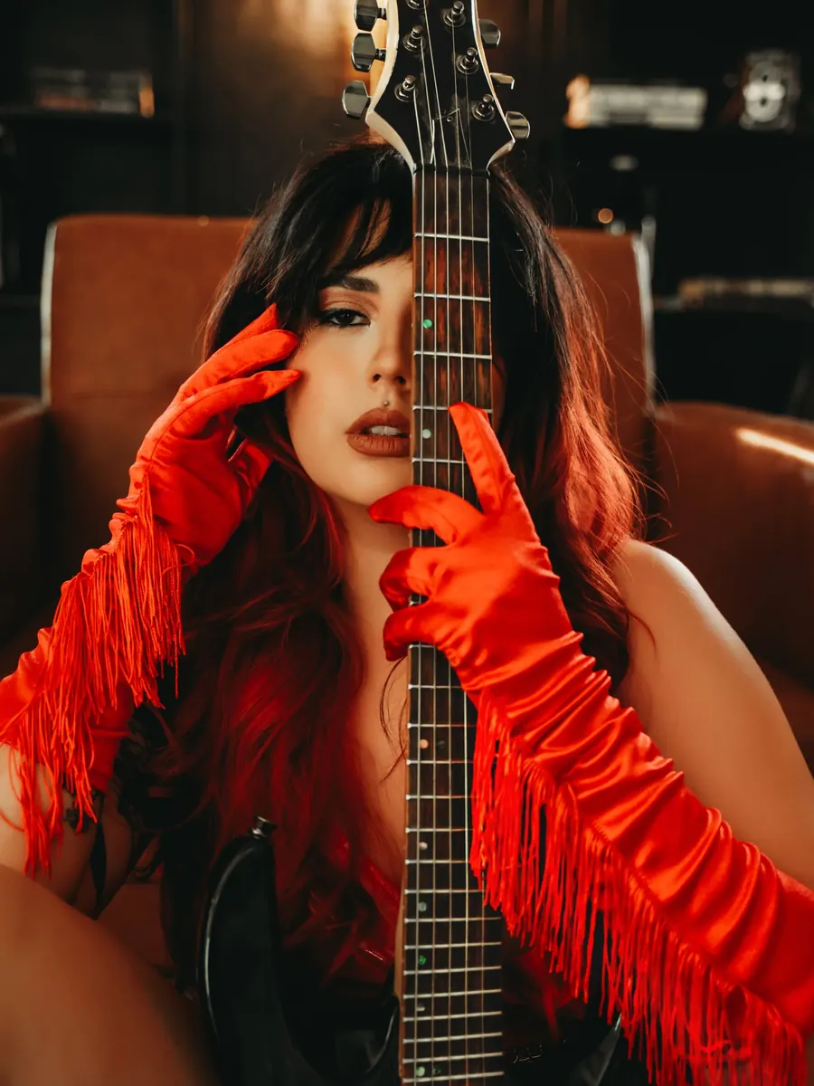Client in long red fringed gloves holding a black electric guitar in a leather chair