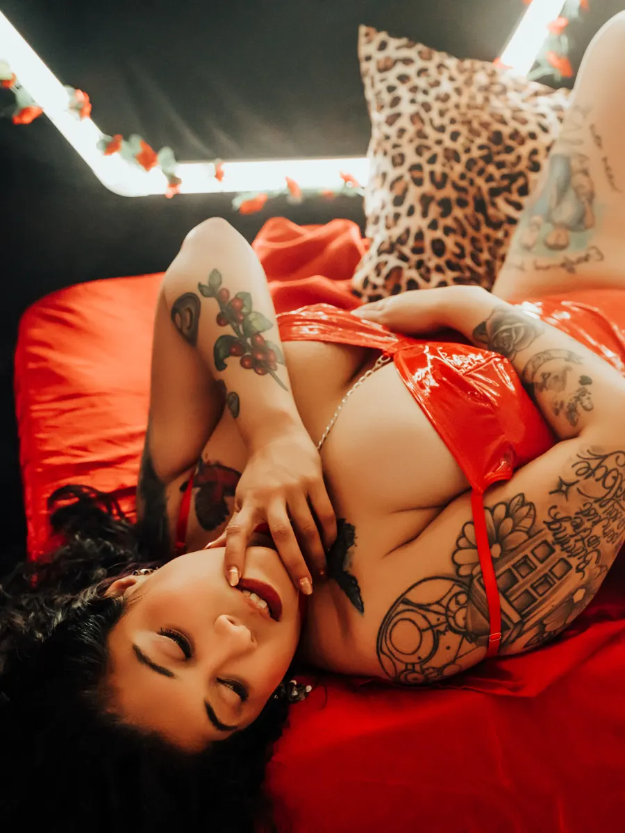 Tattooed client in red lingerie lying on red satin under hexagon light panels