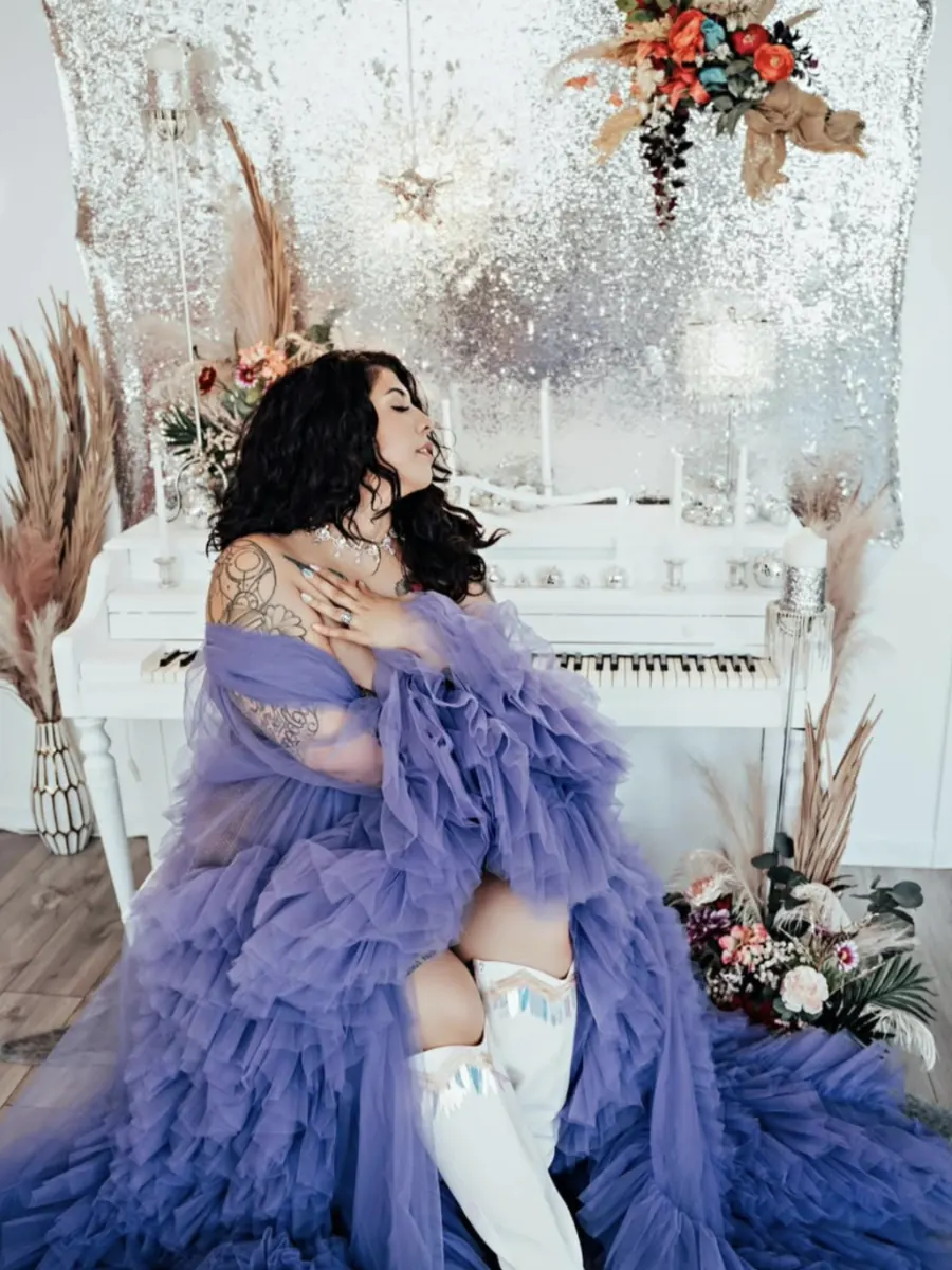Client in a violet tulle robe and white boots seated beside the white studio piano