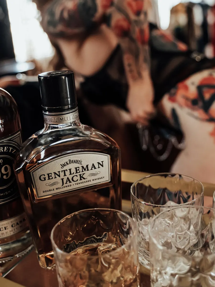 Whiskey bottles and glasses on a gold bar cart, with a client blurred in the background