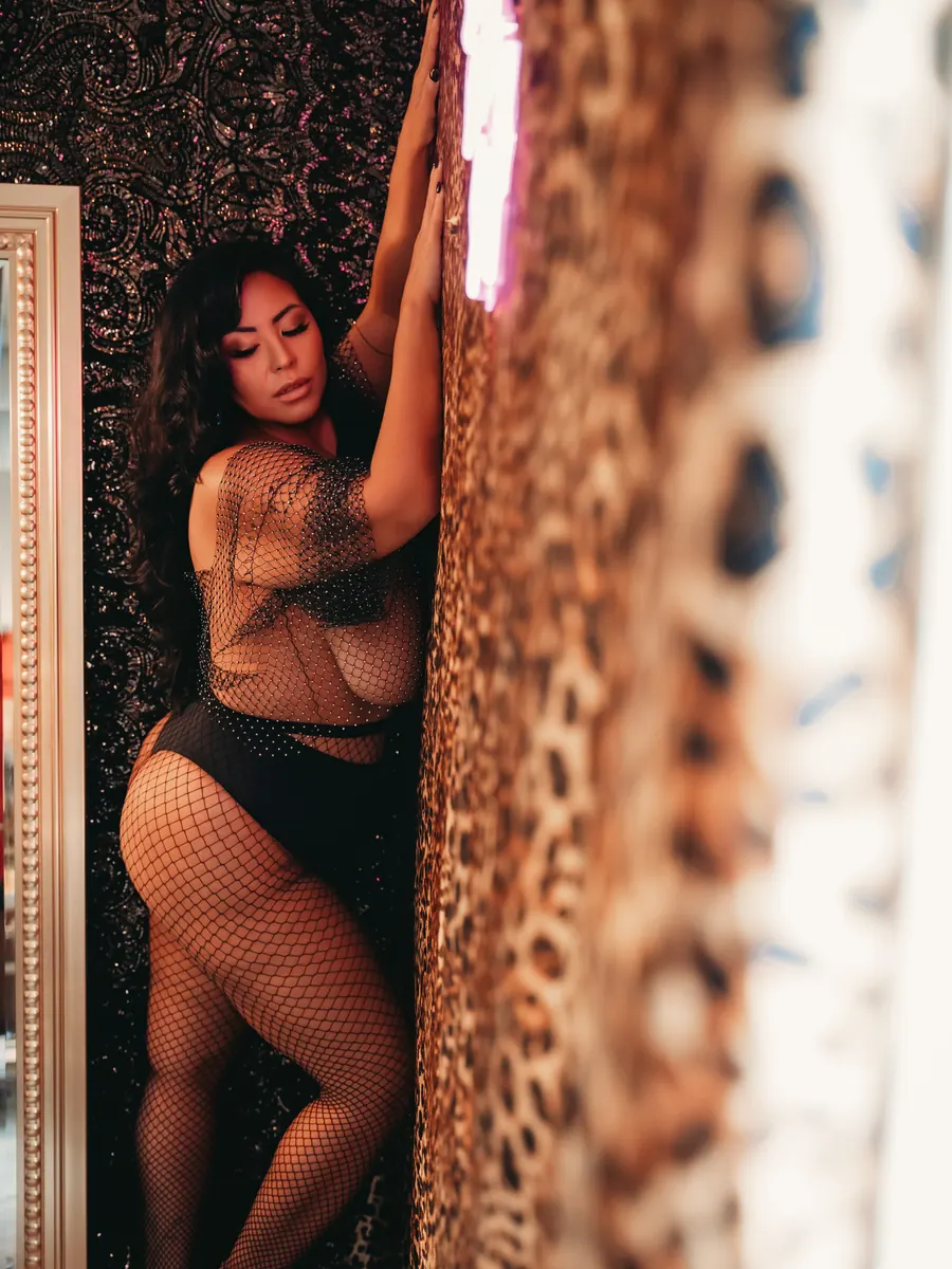 Client in black lace and fishnets leaning against the leopard-print wall